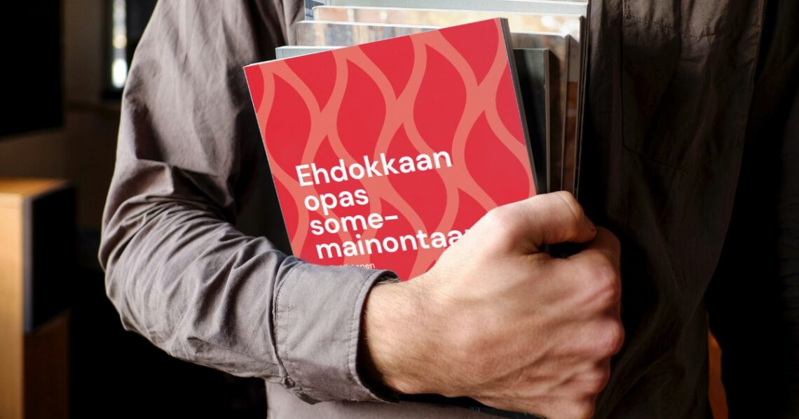 Käsi pitää kainalossa lehtiä, joista päällimmäisessä lukee Ehdokkaan opas somemainontaan.