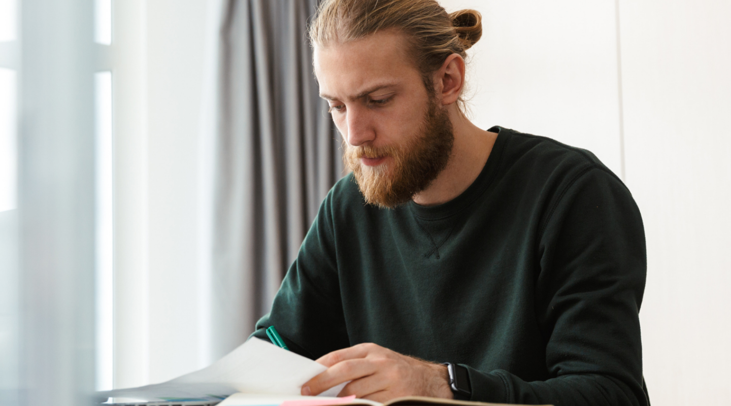 Henkilö istuu pöydän ääressä ja keskittyy paperin lukemiseen.