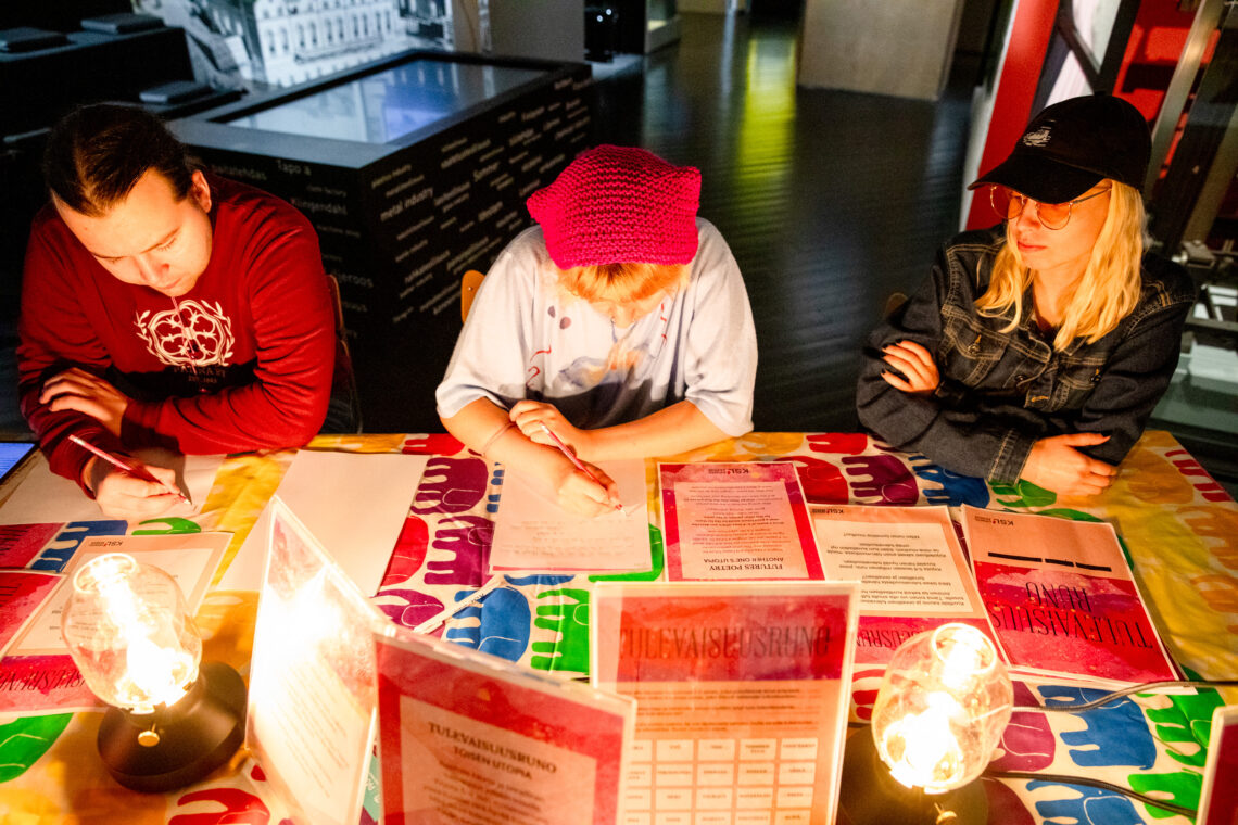 Kolme henkilöä tekee pöydän ääressä Tulevaisuusruno-tehtävää.