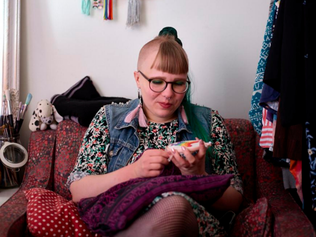 Kevät Sieppi kirjailee sohvalla työtä, jossa on sateenkaari. Kevät Sieppi embroiders a rainbow on the sofa.