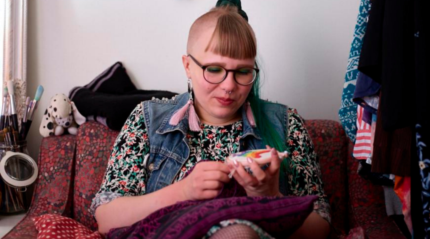 Kevät Sieppi kirjailee sohvalla työtä, jossa on sateenkaari. Kevät Sieppi embroiders a rainbow on the sofa.