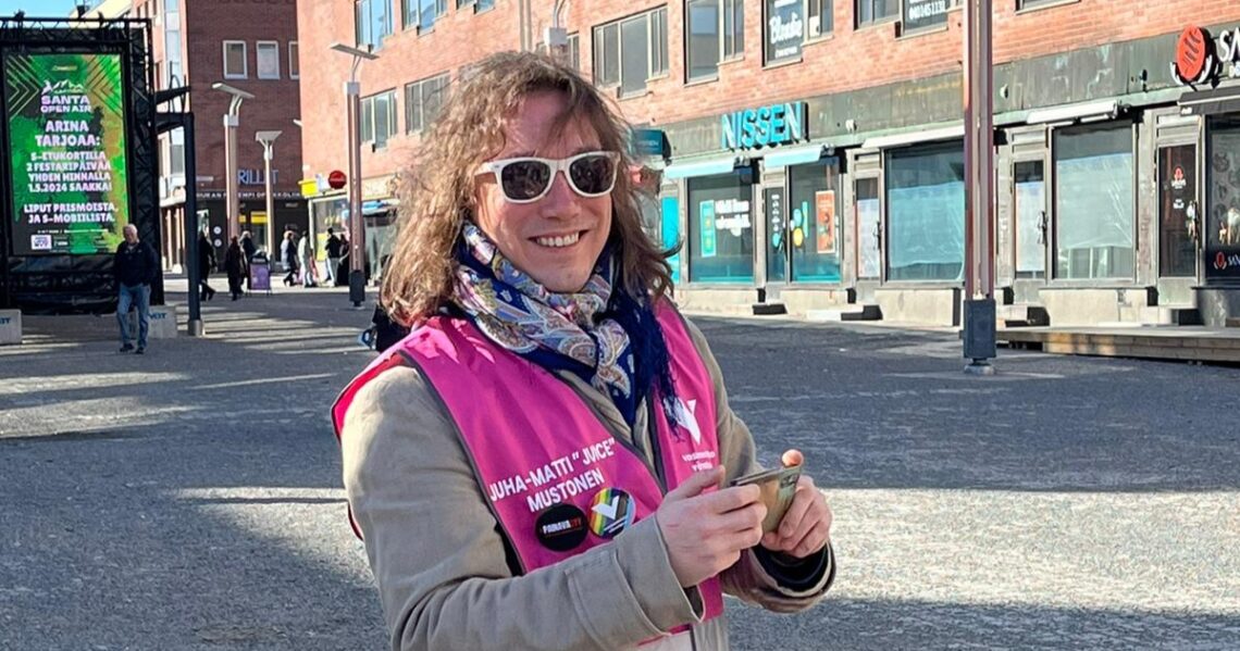 Juha-Matti Mustonen hymyilee vasemmistoliiton kampanjaliivi yllään oululaisella kävelykadulla.