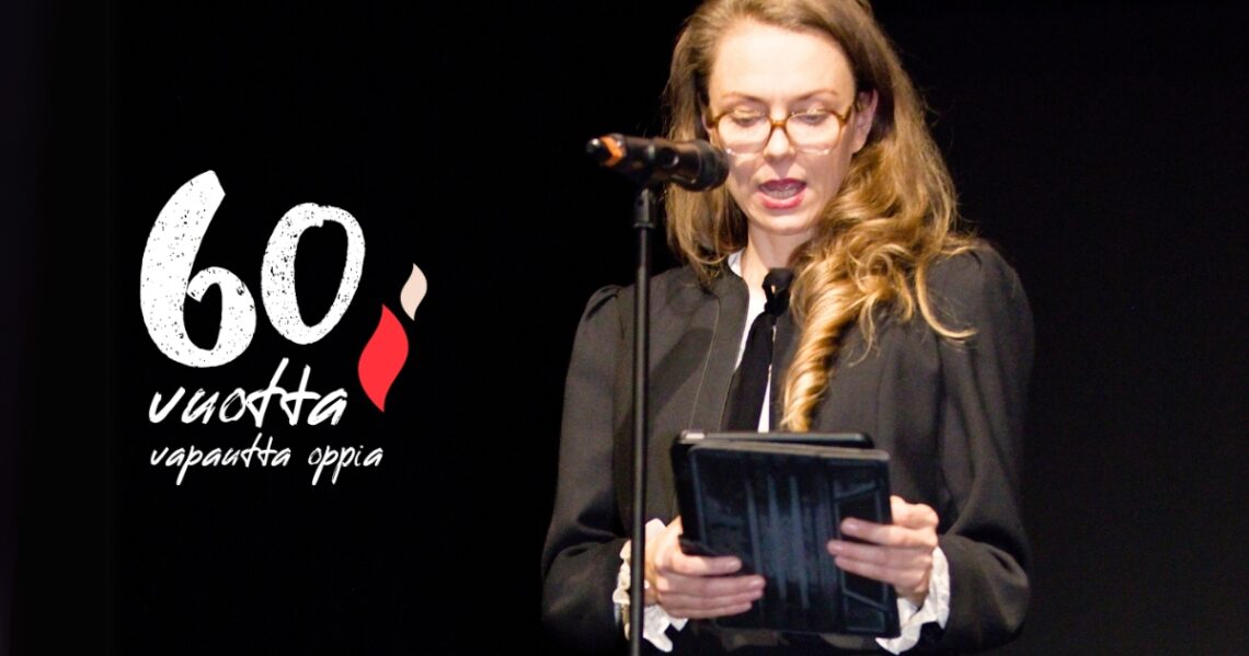 Jenni Pätäri lukee mikrofoniin puhetta tabletilta. Teksti 60 vuotta vapautta oppia!