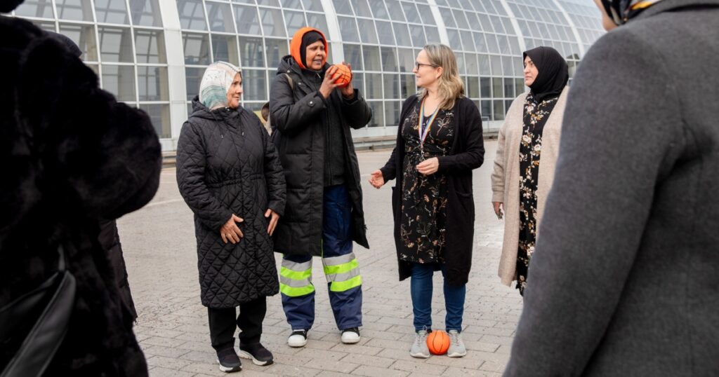 Ryhmä opiskelijoita ja opettaja seisovat ympyrässä Itäkeskuksen pihalla talvitakeissa. Yksi opiskelijoista pitelee palloa ja puhuu, opettajalla on toinen pallo kenkiensä välissä.