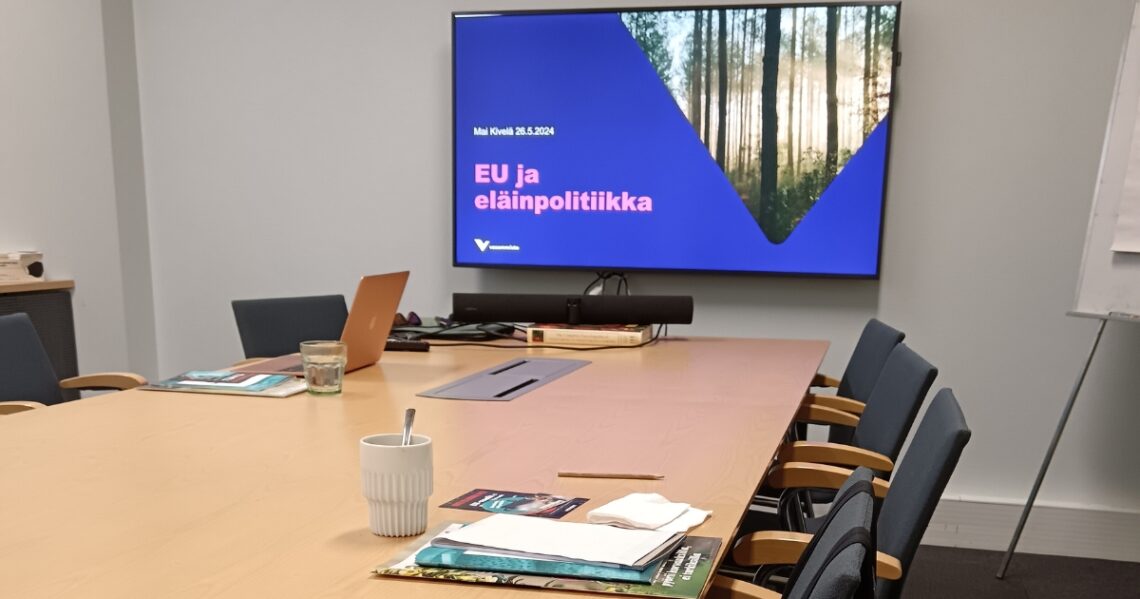 Neuvotteluhuoneessa on diginäyttö, jolla lukee: Mai Kivelä, EU ja eläinpolitiikka, vasemmisto.