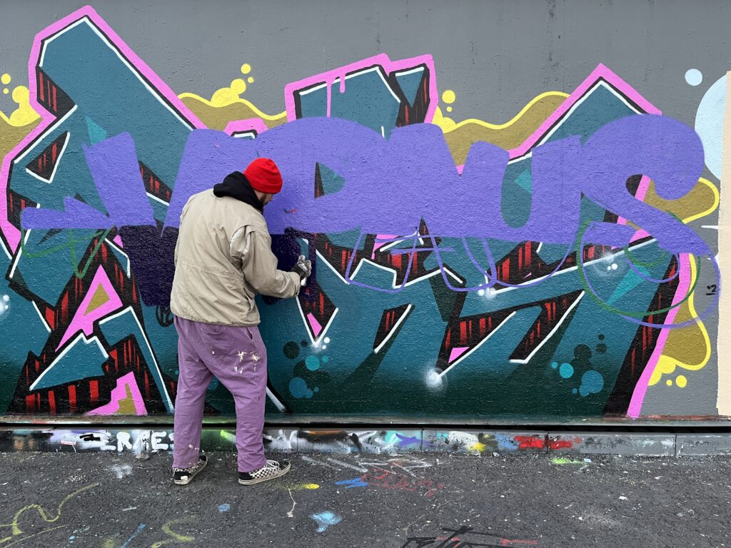 Henkilö maalaa graffitia seinään. Seinälle piirtyy sana vapaus.