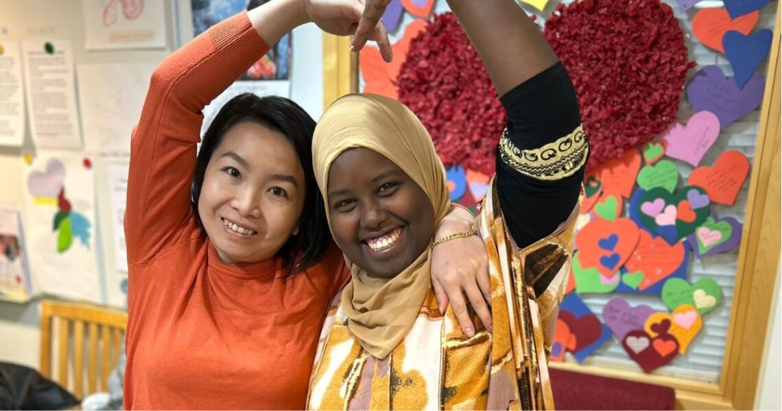 Kaksi henkilöä muodostavat käsillään sydämen ja hymyilevät leveästi.