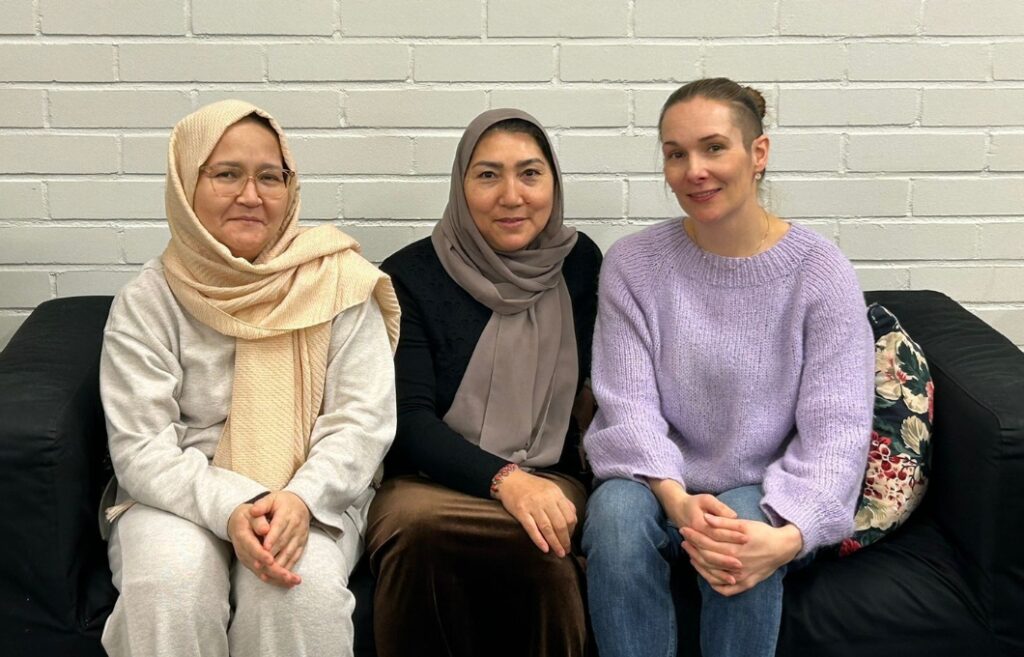 Kolme henkilöä istuu sohvalla ja katsoo kameraan.