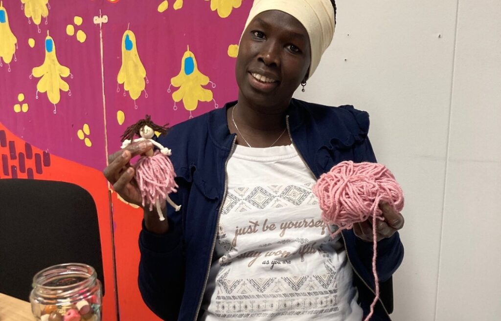 Henkilö istuu pöydän ääressä käsissään lankakerä ja nukke, jolla on lankakerästä valmistettu hame.