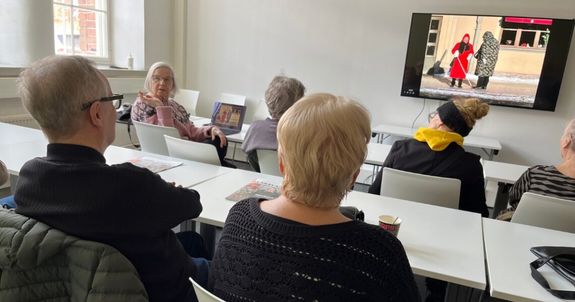 Eläkeläisiä luokkahuoneessa katselemassa näytöltä valokuvia ja keskustelemassa niistä.