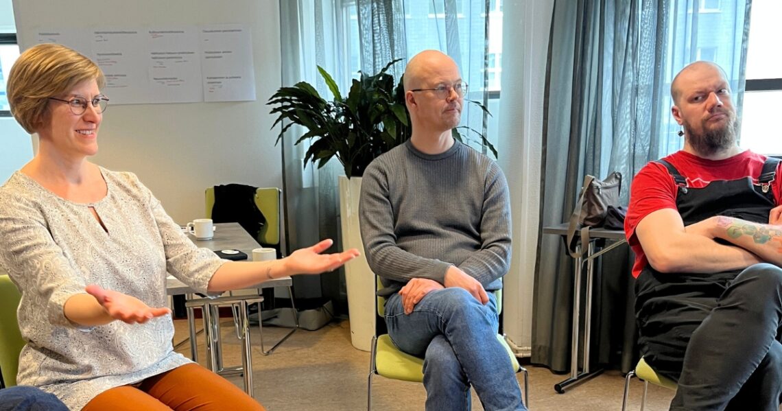 Kolme henkilöä istuu vierekkäin tuoleilla. Ensimmäinen puhuu käsiään levitellen. Toinen kuuntelee neutraalisti. Kolmas pohtii kriittisesti kuulemaansa.