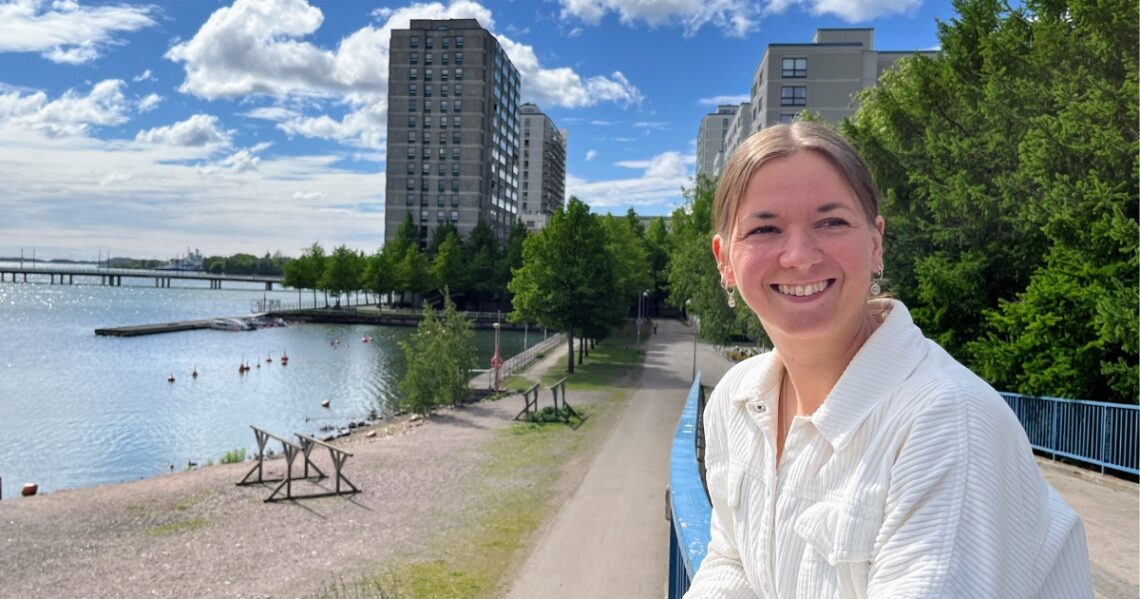 Emmi Paananen nojaa sillan kaiteeseen Merihaassa Helsingissä. Taustalla näkyy vihreitä puita, kerrostaloja ja meri.