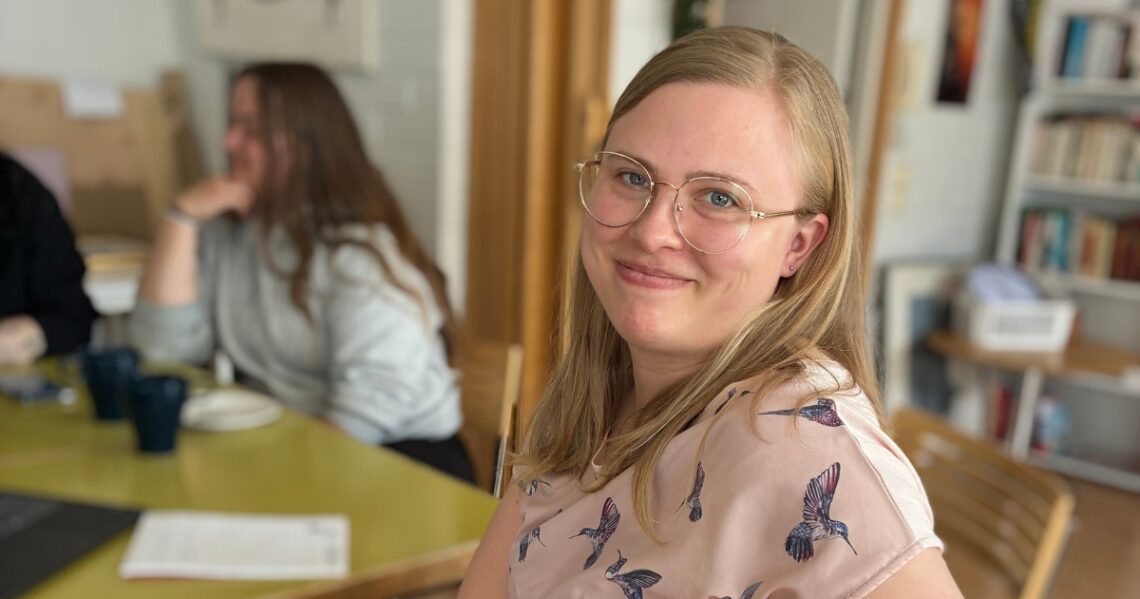 Opiskelija katsoo hymyillen kameraan luokkatilassa.