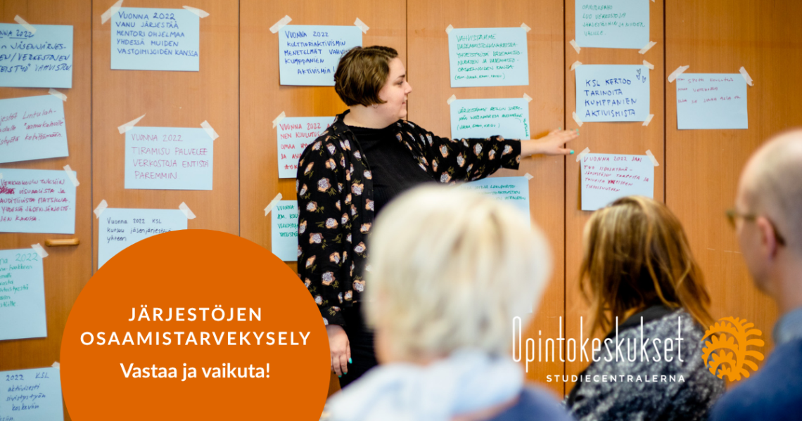 Henkilö puhuu ja osoittaa seinälle kiinnitettyä paperia, johon on tussilla kirjoitettu tekstiä. Seinällä on paljon vastaavia papereita, muut kuuntelevat.